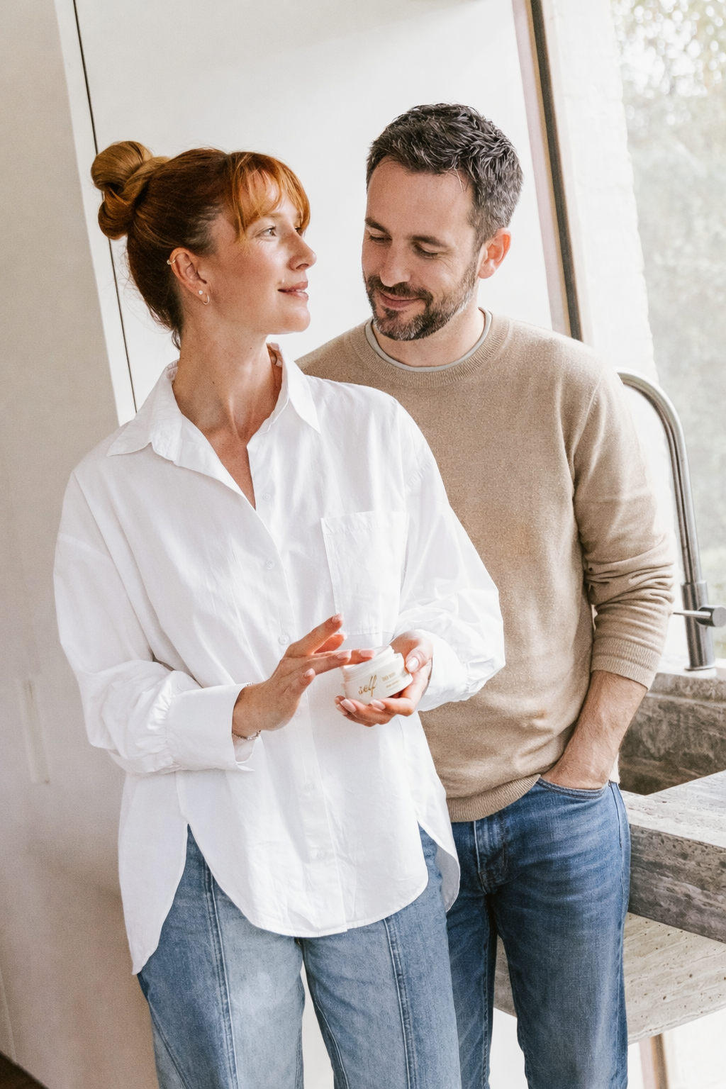 Een koppel houdt samen een pot Self body butter vast in een lichte Belgische keuken
